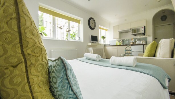 Un dormitorio con cama, almohadas y vistas a una cocina y zona de estar.