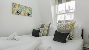 Une chambre d’hôtel avec deux lits, du linge de lit blanc, plusieurs oreillers, une fenêtre donnant sur des immeubles et une œuvre d’art florale accrochée au mur.