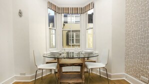 Un coin repas comprenant une table ronde en verre, quatre chaises blanches et un banc en bois.