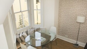 Un espace repas moderne avec une table en verre, des chaises blanches et un papier peint à motifs.