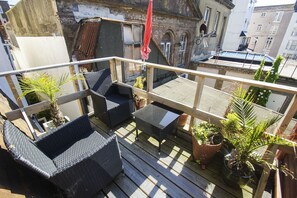 Une terrasse sur le toit, aménagée avec des meubles en osier, des plantes en pot et un parasol rouge.