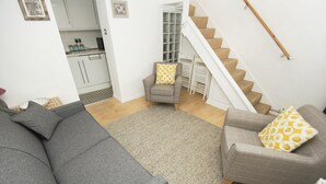 A living room with a grey sofa, a patterned armchair, and a staircase leading to a kitchen.