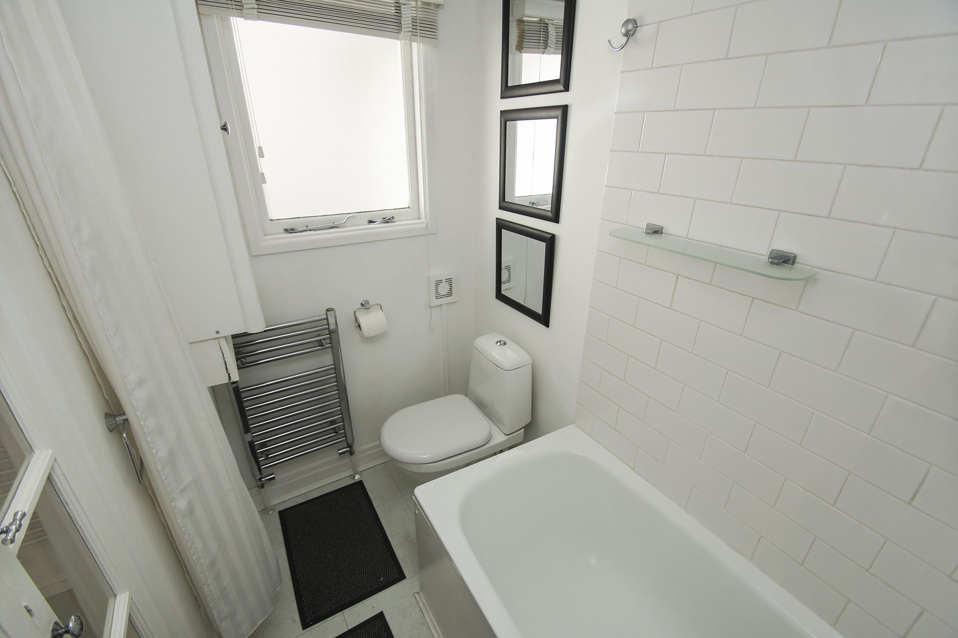 A small, white bathroom with a toilet, a bathtub, a window, and a mirror.