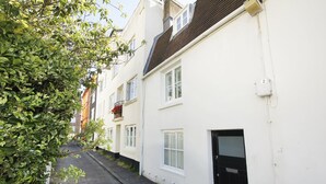 A narrow street with white buildings, a black door, and a small window with shutters.