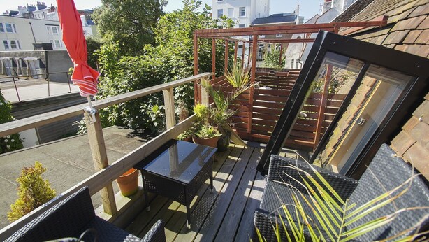 A balcony with a glass door, wooden railing, and potted plants.