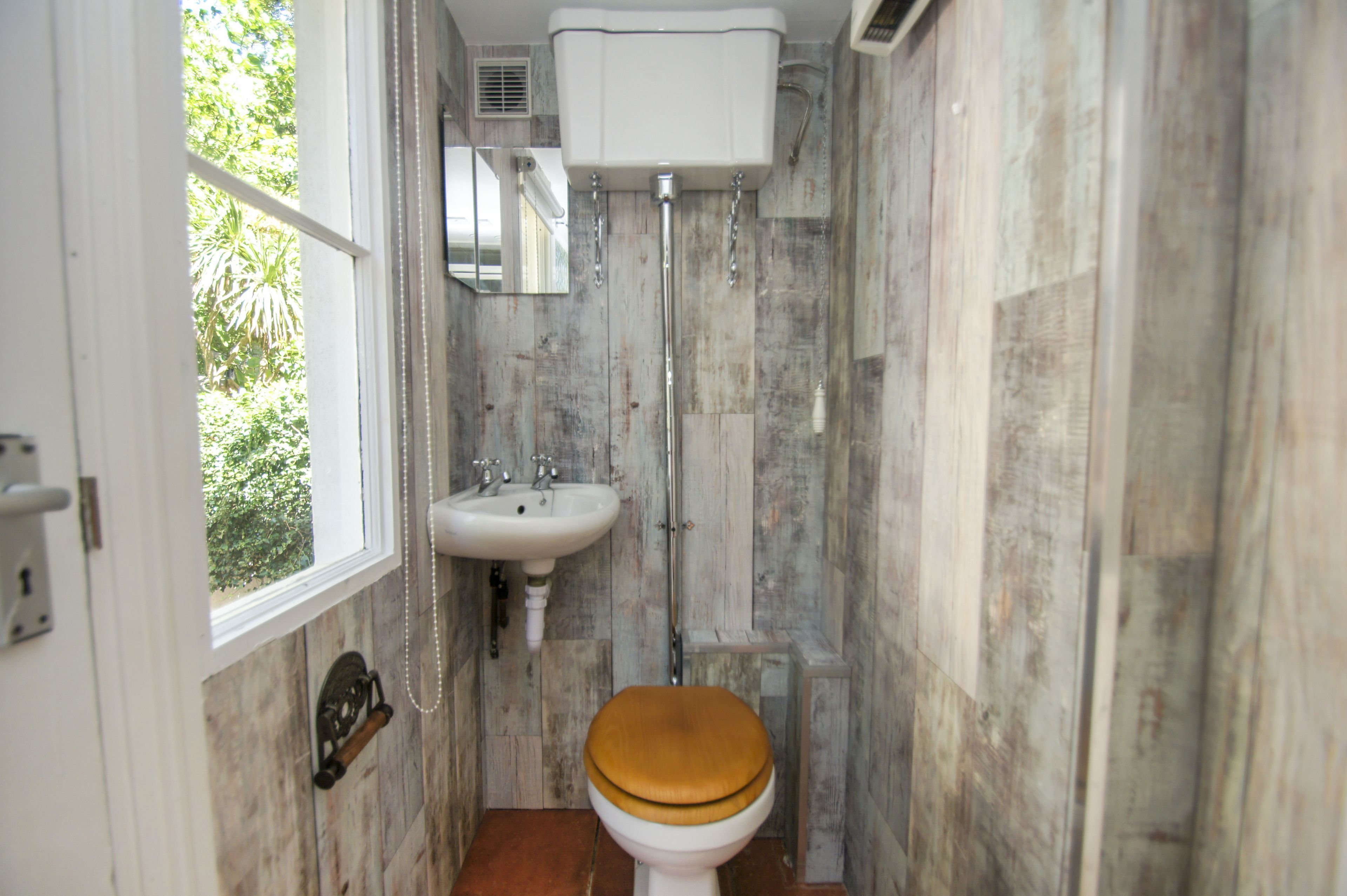 A small bathroom with a wooden wall, a white sink, and a wooden toilet.