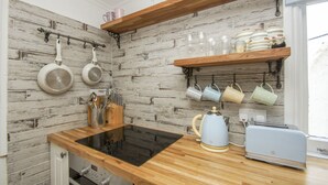 A kitchen with a wooden countertop, a black induction cooktop, a kettle, a toaster, and hanging utensils. - Brunswick Garden Studio Patio by Brighton Holiday Lets (Hove)