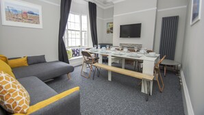 Een moderne woonkamer met een grijze bank, een eettafel gedekt voor vier personen en een groot raam met gordijnen.