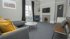 Een moderne woonkamer met grijze banken, een ronde salontafel, een open haard en een flatscreen televisie.