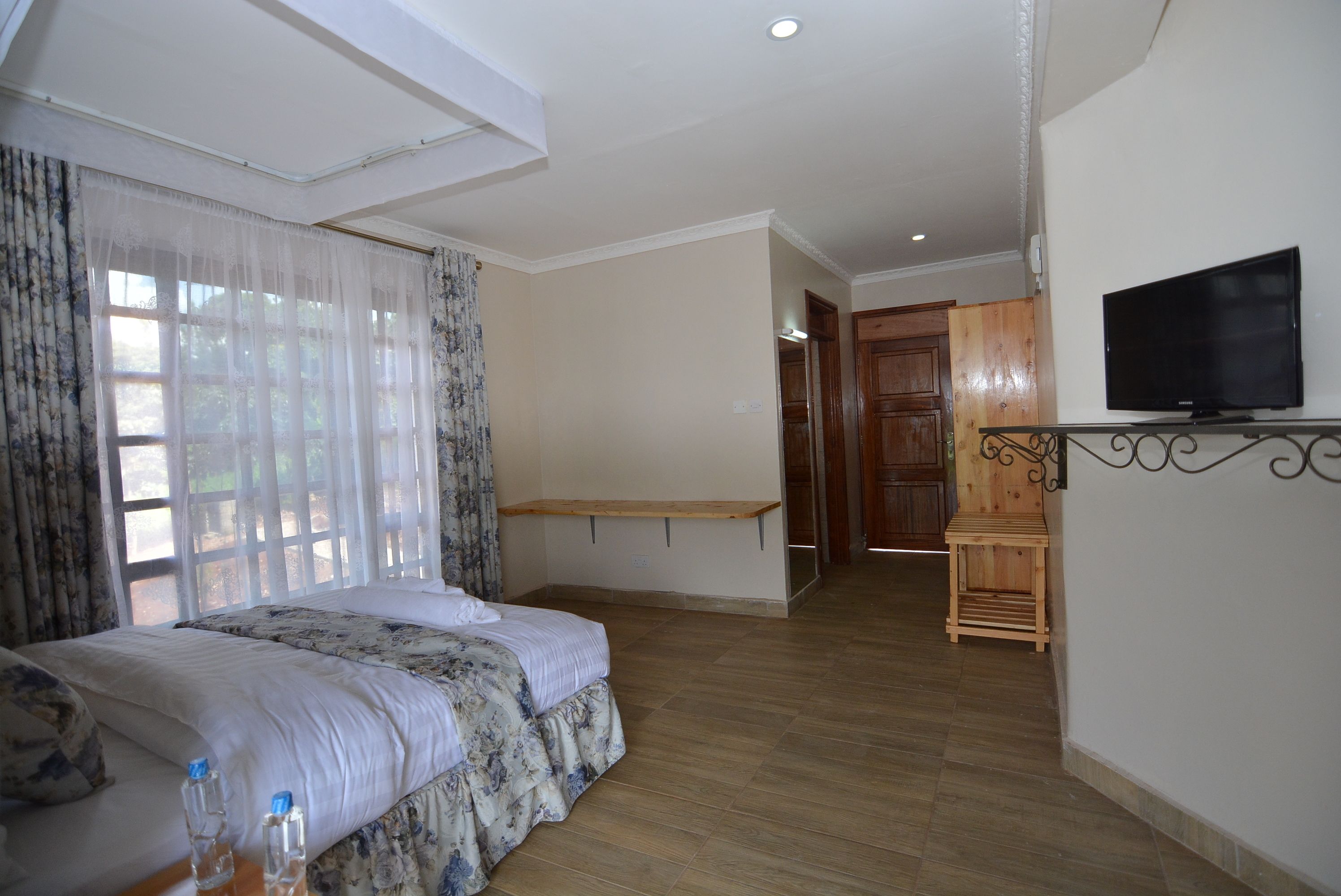 A hotel room with a bed, a TV, a wooden bench, and a TV stand.