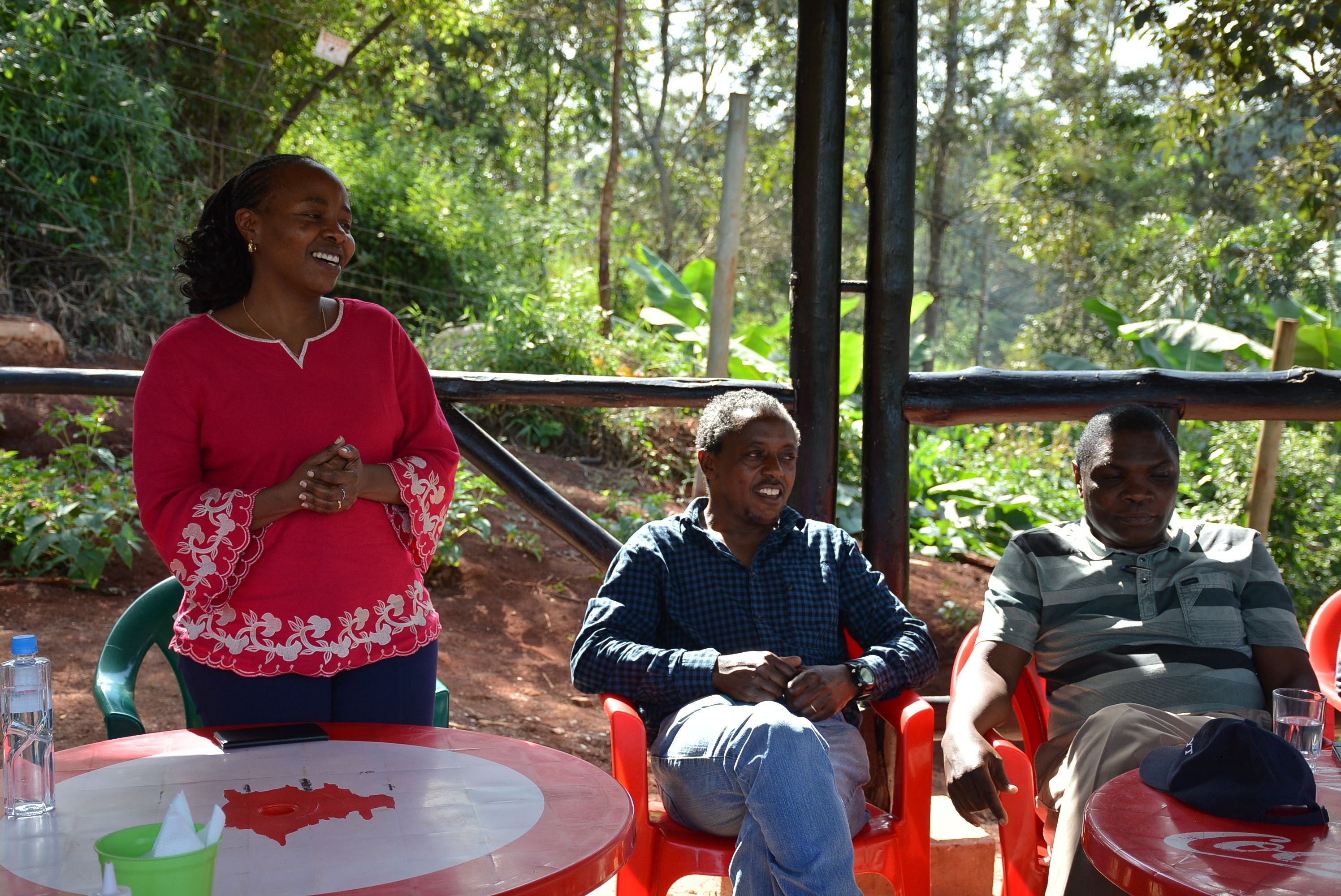 Three people seated at a round table outdoors with a natural backdrop.