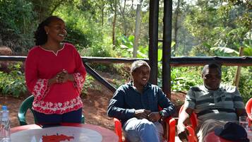 Three people seated at a round table outdoors with a natural backdrop.