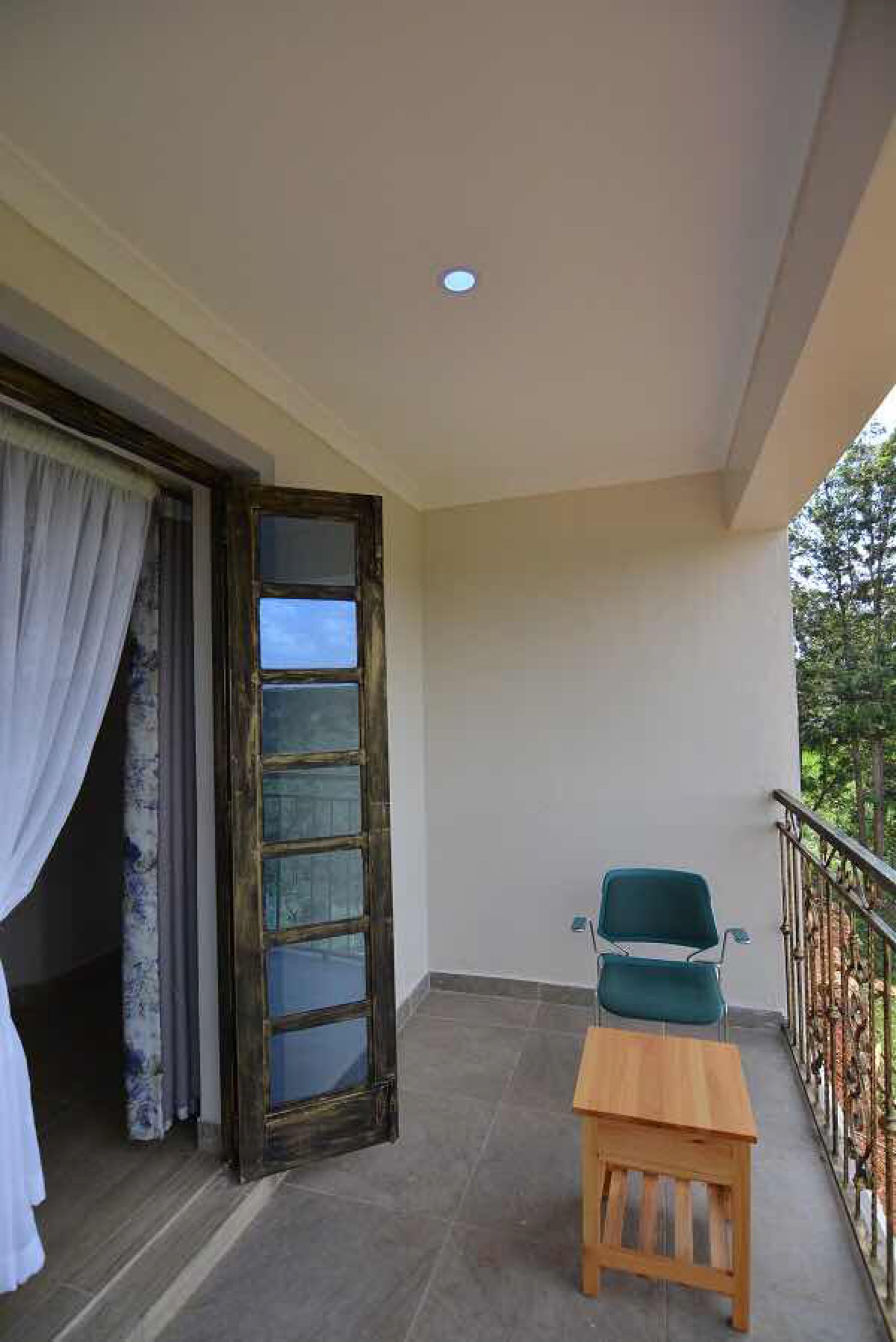 A balcony with a wooden table and a green chair, a glass door, and a view of trees.
