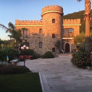 Un château en pierre doté d’une tour ronde, d’une cour pavée et entouré de verdure.