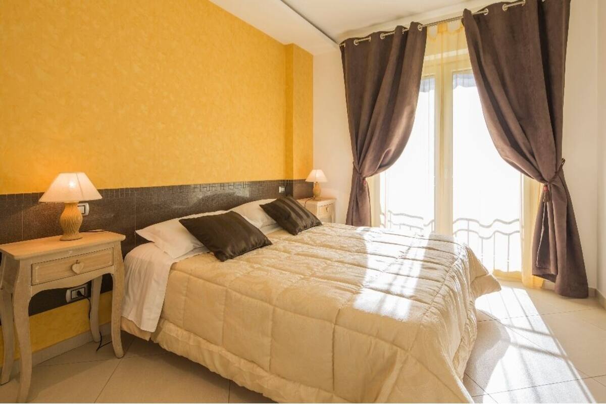 Una habitación de hotel con una cama, dos mesitas de noche, una lámpara y una ventana con cortinas.