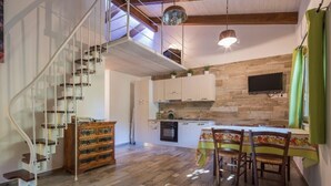 A spacious kitchen with wooden flooring, a dining area with a table and chairs, and a spiral staircase leading to an upper level.