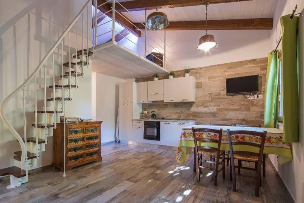 Cocina amplia con piso de madera, comedor con mesa y sillas, y escalera en espiral que conduce a un nivel superior.
