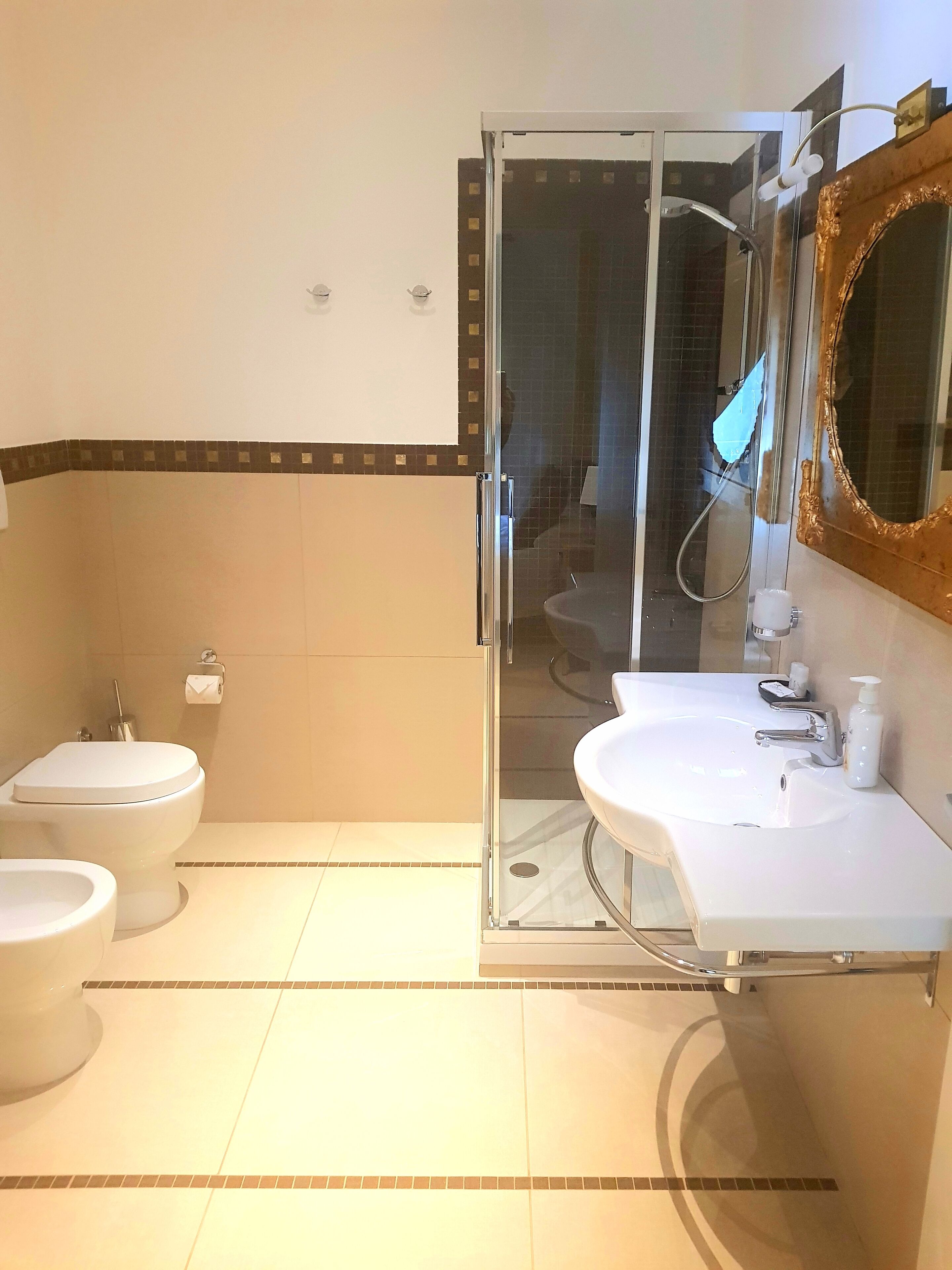 Une salle de bain avec une douche à parois de verre, deux toilettes, un lavabo avec un miroir et un distributeur de serviettes.