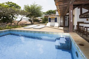 A swimming pool with a tiled edge, lounge chairs, and a wooden deck.