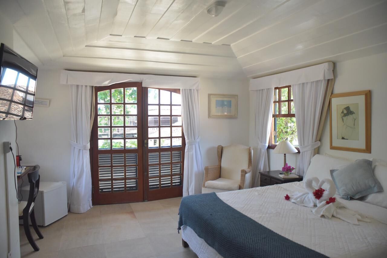 Quarto com cama, cadeira, escrivaninha e janela com cortinas.