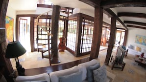 A spacious living area with a wooden ceiling, a sofa with patterned cushions, a television, and a guitar. - Pousada Blanca Mar - Praia do Canto (Búzios)