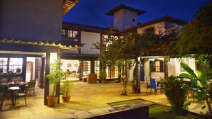 A courtyard with outdoor seating, potted plants, and a building with a tiled roof. - Pousada Blanca Mar - Praia do Canto (Búzios)