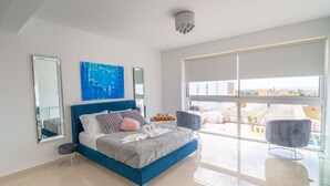 Une chambre moderne avec un grand lit, une tête de lit bleue, une grande fenêtre donnant sur un beau paysage et un miroir sur le mur.