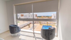 Une pièce dotée d’une grande fenêtre donnant sur une piscine et un quartier résidentiel. On y trouve deux fauteuils modernes.