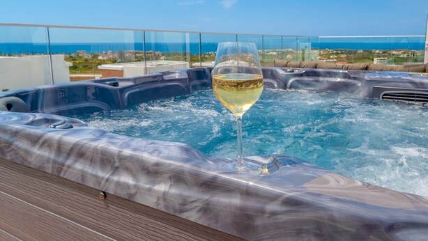 Un bain à remous avec un verre de vin blanc, installé sur une terrasse en bois offrant une vue imprenable sur la côte.