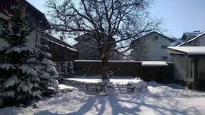 A snow-covered courtyard with a large tree, stone walls, and traditional buildings. - Winter Chalet fully catered - Pirin Adventures - Bansko - Bulgaria 8-12 people (Bansko)