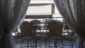 Ein Essbereich mit Tisch und Stühlen, Vorhänge mit floralem Muster und Blick auf ein Gebäude mit Balkon.