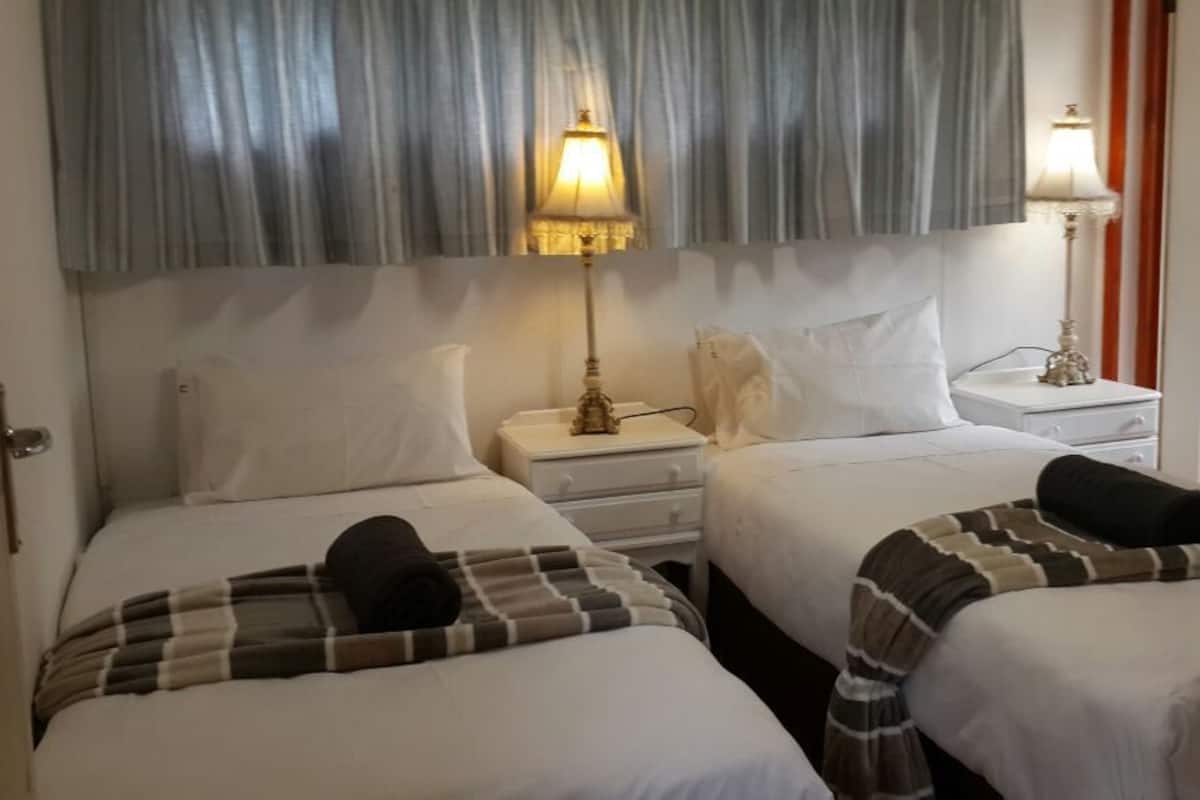 Een hotelkamer met twee bedden, elk met een kussen en dekbed. Er staan twee nachtkastjes met lampen.