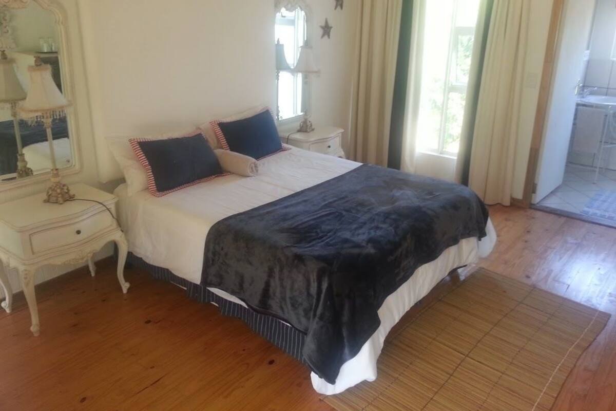 Een slaapkamer met een groot bed, een nachtkastje, een dressoir, een spiegel en een raam met gordijnen.