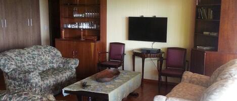 Una sala de estar con sofás de estampado floral, una mesa de centro, un televisor y armarios de madera.