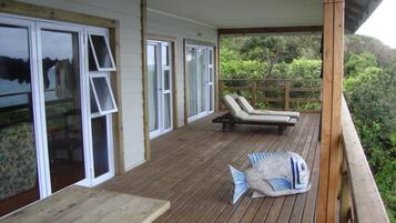 Relax on the deck with two lounge chairs and a wooden table, surrounded by a lush landscape.