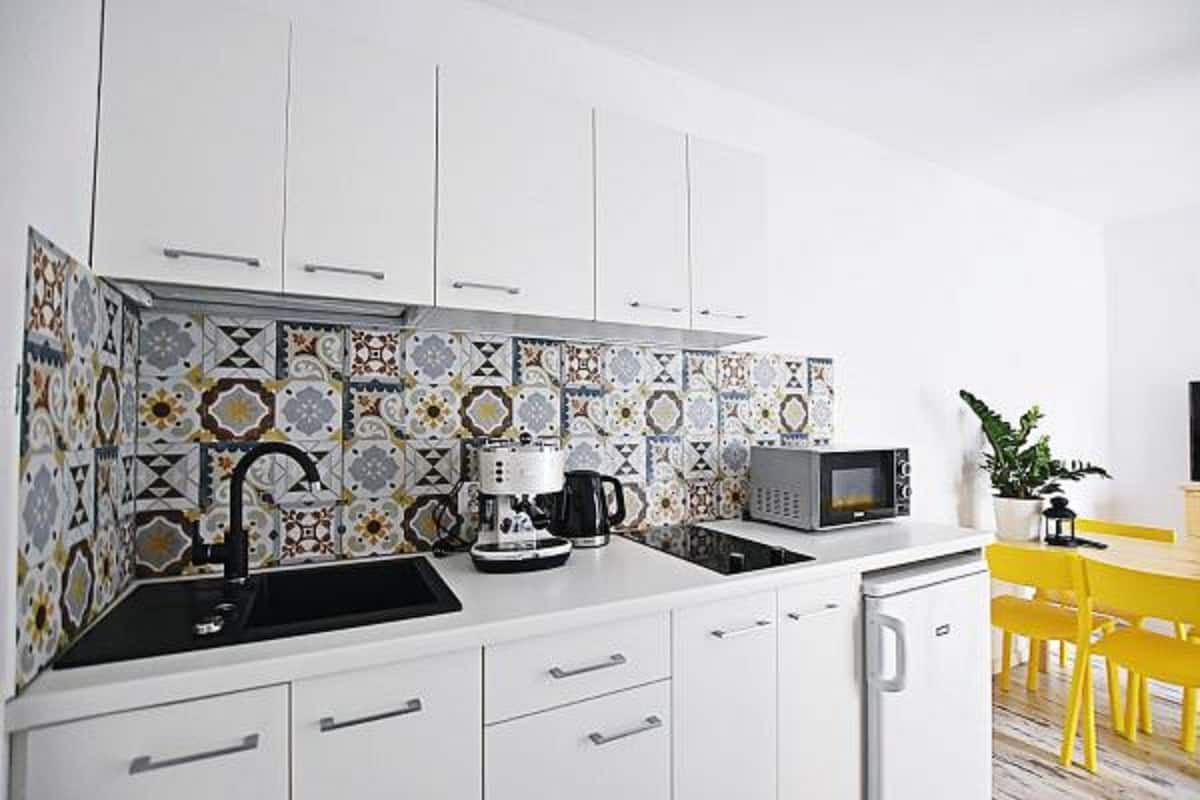 A compact kitchen with white cabinets, a black sink, a coffee maker, and a microwave.