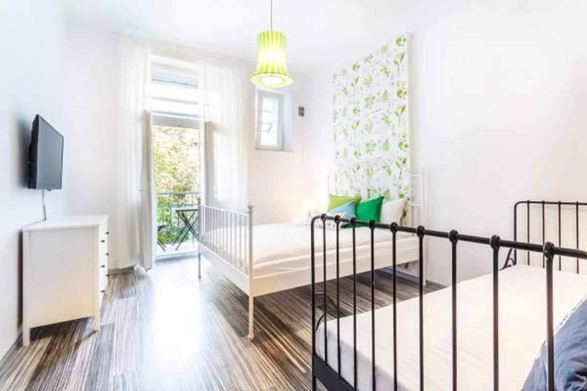 A bedroom with a bed, a bedside table, a TV, and a window with a view of greenery.
