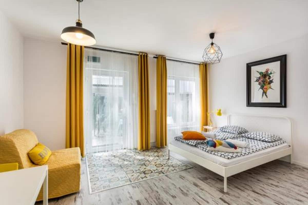 A modern bedroom with a white bed, yellow curtains, a yellow armchair, and a patterned rug.