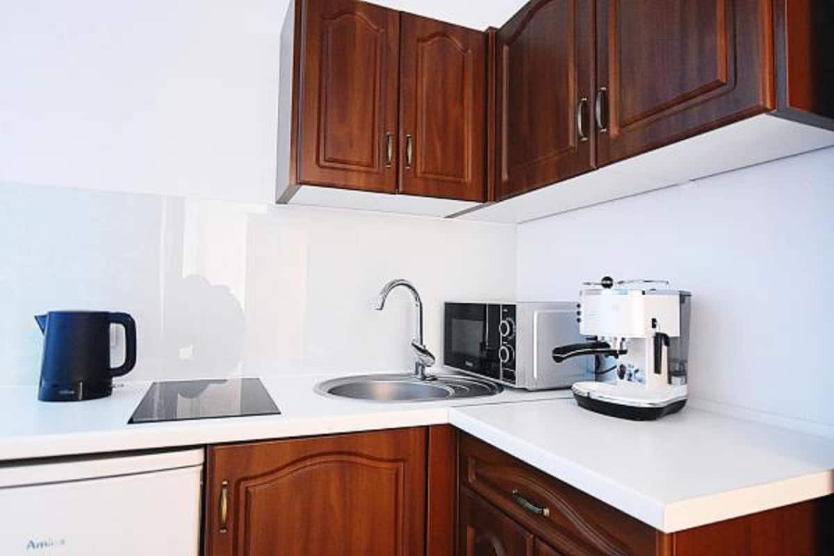A modern kitchen with wooden cabinets, a sink, a kettle, a microwave, and a coffee maker.