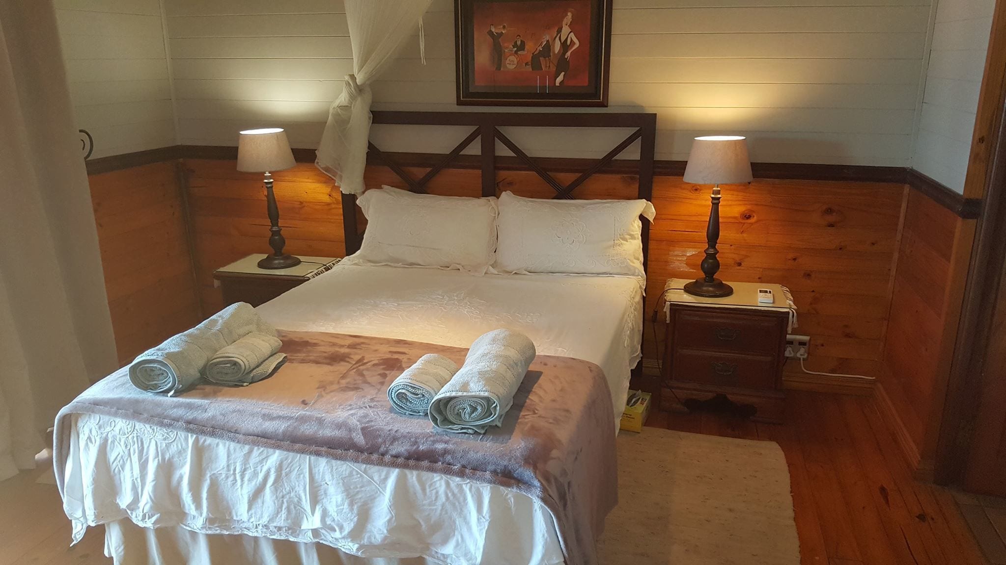 Een keurig opgemaakt bed met twee kussens, een hoofdbord en twee nachtkastjes met lampen.
