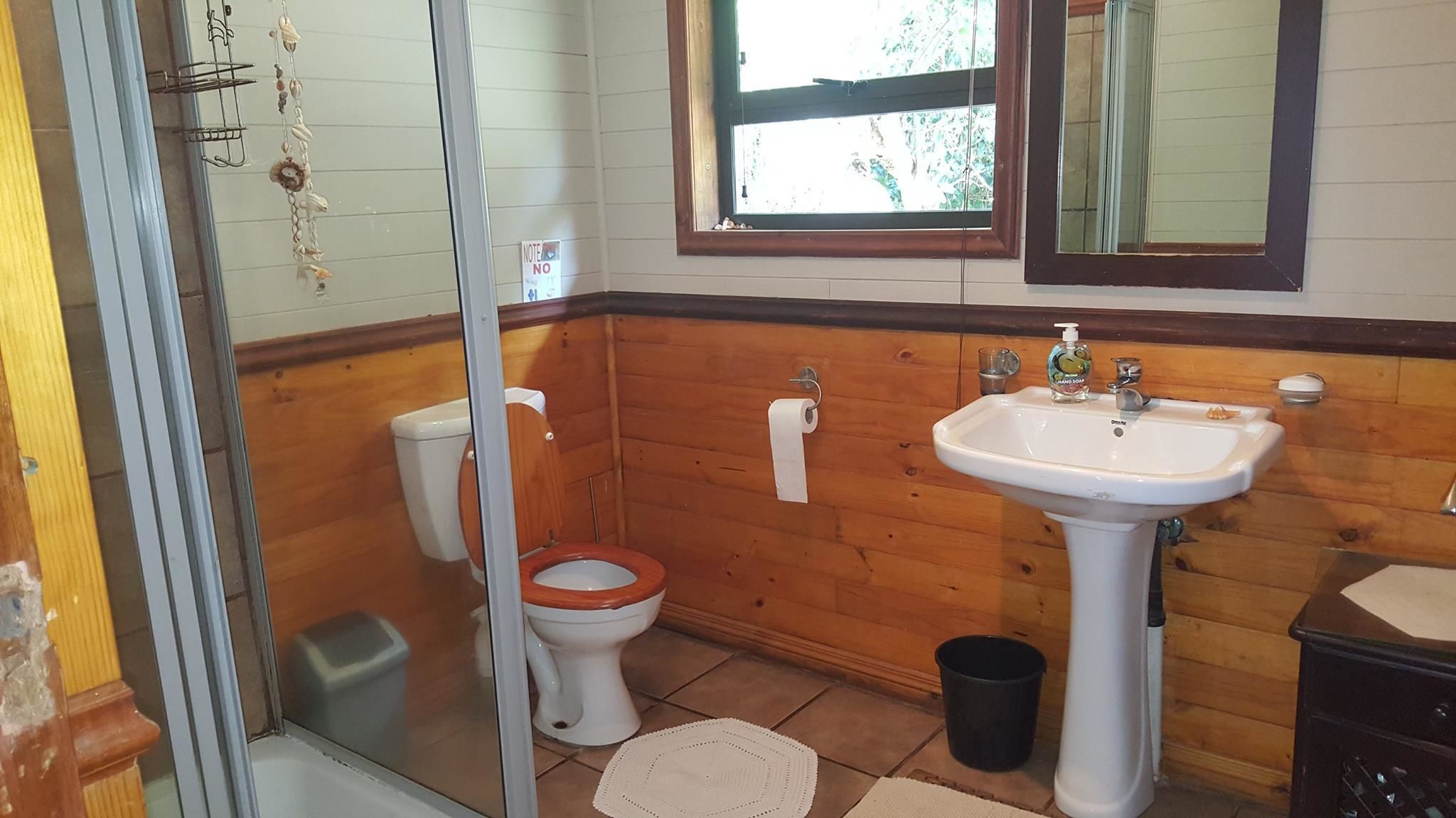 Un baño con paneles de madera, un lavabo blanco, un inodoro y una zona de ducha.