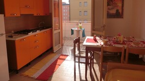 A compact kitchen with orange cabinets and a dining area with a table and chairs. - Condominio Lero (San Michele al Tagliamento)