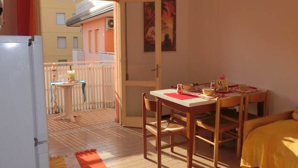 A small, cozy room with a wooden table and chairs, a bed with a yellow cover, and a view of a building outside. - Condominio Lero (San Michele al Tagliamento)