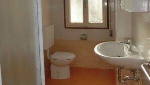 A small bathroom with a toilet, sink, and window. - Condominio Lero (San Michele al Tagliamento)