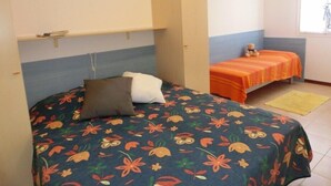 A bedroom with a bed, a nightstand, a window, and a small table. - Condominio Lero (San Michele al Tagliamento)