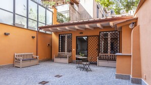 An outdoor patio with a tiled floor, a wooden bench, a small table with a chair, and a security camera. - Residenza Palline by Hili (Rome)