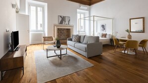 A spacious living room with a wooden ceiling, a fireplace, a sofa, a coffee table, and a dining area with chairs. - Residenza Palline by Hili (Rome)