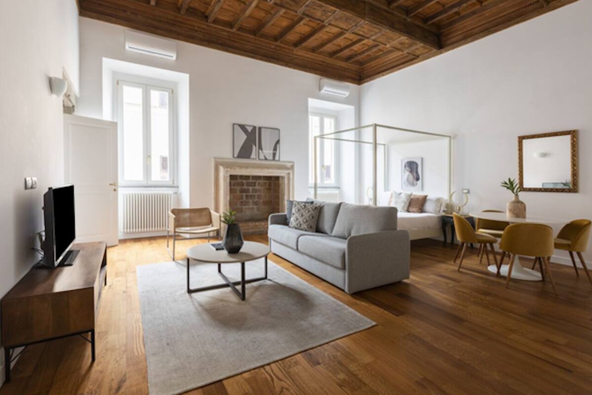 A spacious living room with a wooden ceiling, a fireplace, a sofa, a coffee table, and a dining area with chairs.