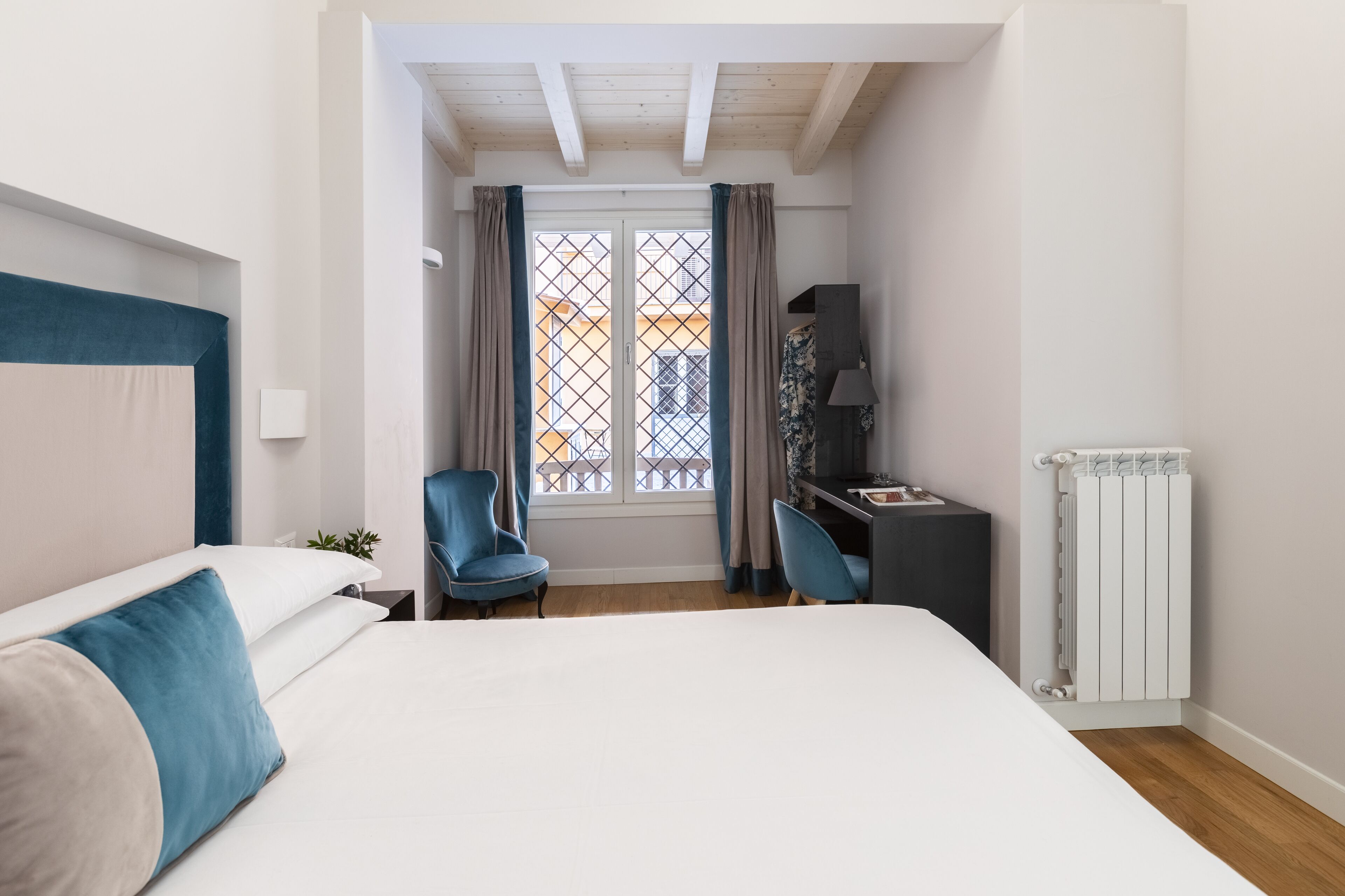 A bedroom with a bed, a desk, a chair, a radiator, and a window with curtains.