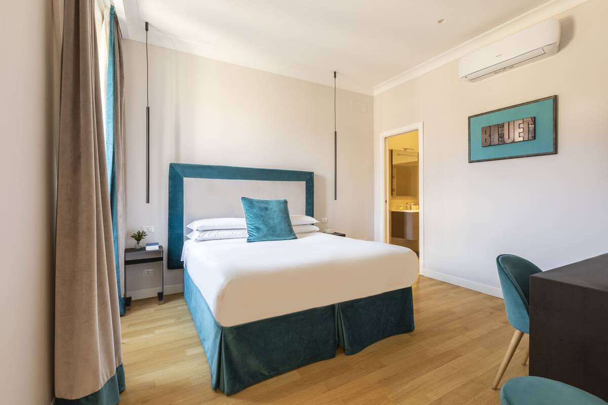 A modern hotel room with a large bed, a bedside table, a desk, and a chair.